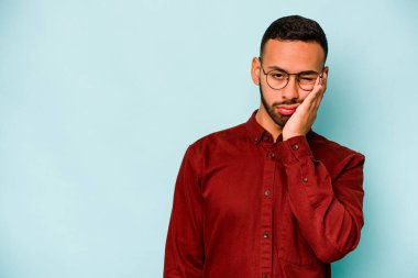 Mavi arka planda izole edilmiş, üzgün ve dalgın hisseden genç bir İspanyol fotokopi odasına bakıyor..