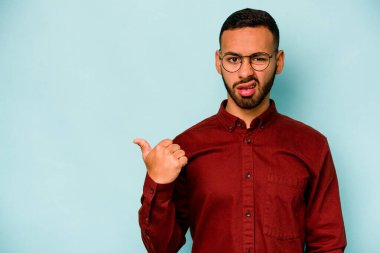 Mavi arka planda izole edilmiş genç İspanyol adam işaret parmağıyla fotokopi alanını işaret ederek şok oldu..