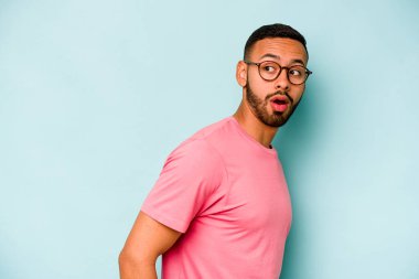 Mavi arka planda soyutlanmış genç bir İspanyol gülümsüyor, neşeli ve keyifli görünüyor..