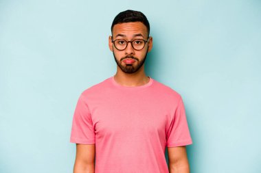 Genç İspanyol adam mavi arka planda izole edilmiş üzgün, ciddi yüz, mutsuz ve hoşnutsuz hissediyor.