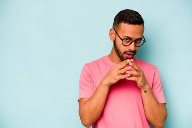 Latin kökenli genç bir adam mavi arka planda izole edildi. Aklında bir plan kuruyor, bir fikir kuruyor..