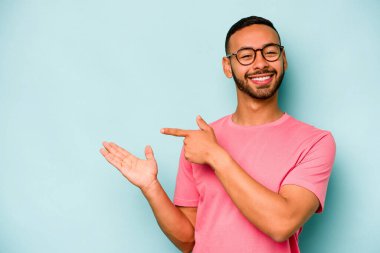 Mavi arka planda izole edilmiş genç İspanyol bir adam heyecanlı bir şekilde avuç içinde bir kopyasını tutuyor..