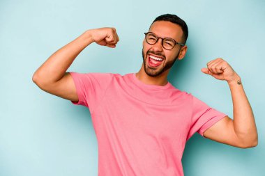 Mavi arka planda izole edilmiş genç İspanyol bir adam zaferden sonra yumruk kaldırıyor, kazanan konsept..