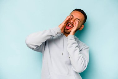 Genç İspanyol adam mavi arka planda izole edilmiş, heyecanlı bir şekilde bağırıyor..