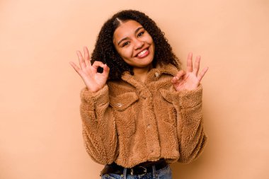 Genç Afrikalı Amerikalı kadın bej arka planda izole edilmiş neşeli ve kendinden emin, iyi bir hareket sergiliyor..