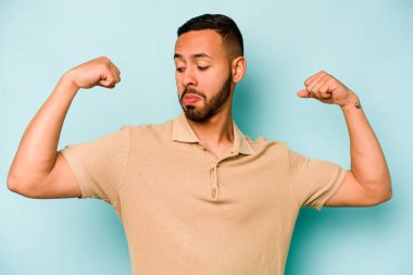 Mavi arka planda izole edilmiş genç bir İspanyol kadın gücünün sembolü olan kollarıyla güçlü bir hareket gösteriyor.