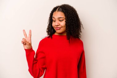 Beyaz arka planda izole edilmiş genç Afrikalı Amerikalı kadın neşeli ve kaygısız parmaklarıyla barış sembolü gösteriyor..