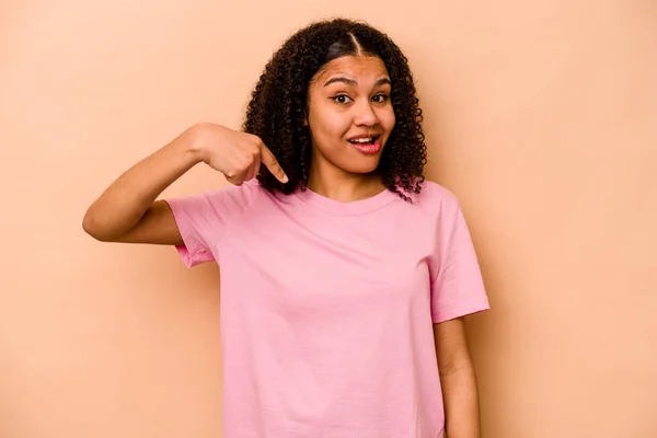 若いアフリカ系アメリカ人の女性は ベージュの背景の人に手でシャツのコピースペースを指して孤立し 誇りと自信を持って — ストック写真