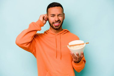 Mavi arka planda izole edilmiş erişte yiyen genç İspanyol kadın elleriyle kulaklarını kapatıyor..