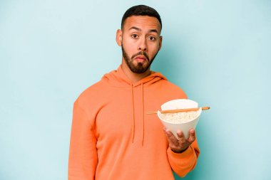 Mavi arka planda izole edilmiş erişte yiyen genç İspanyol kadın omuzlarını silker ve gözleri açık kalır..