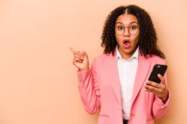 Elinde cep telefonu olan genç Afrikalı Amerikalı bir kadın bej arka planda izole edilmiş olarak kenarı işaret ediyor.