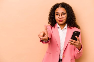 Elinde cep telefonu olan genç Afrikalı bir kadın bej arka planda bir numarayı parmağıyla gösteriyor..