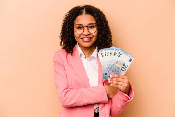 Young African American business woman holding banknotes isolated on beige background laughing and having fun.