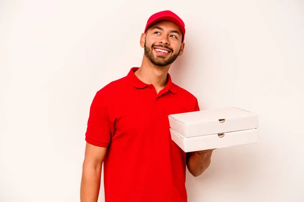 白い背景に隔離されたピザを持っている若いヒスパニック系の配達人は脇笑顔 陽気で楽しい見えます — ストック写真