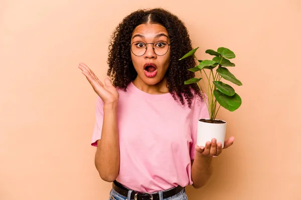 Young African American Woman Holding Plant Isolated Beige Background Surprised — Stock fotografie