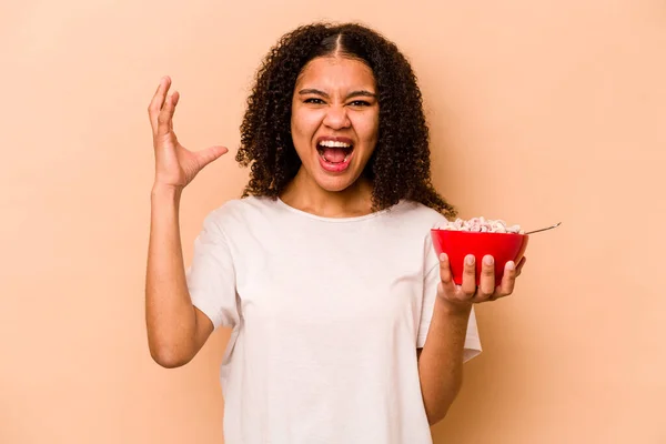 年轻的非洲裔美国女人拿着一碗米黄色背景的谷类食品 惊喜极了 兴奋地举起双手 — 图库照片