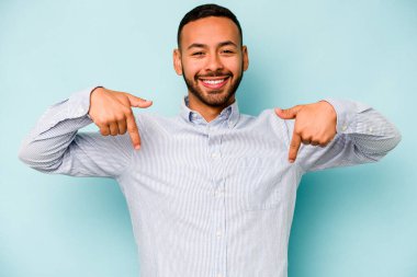 Genç İspanyol bir adam mavi arka planda izole edilmiş. Parmakları aşağıda, olumlu hisler içinde..