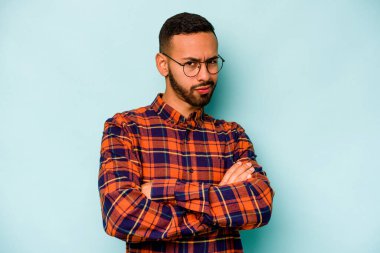 Genç İspanyol bir adam mavi arka planda izole edilmiş şüpheli, belirsiz, seni muayene ediyor..