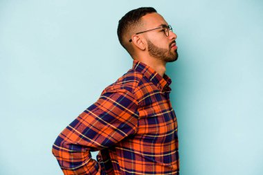 Genç İspanyol bir adam mavi arka planda izole edilmiş sırt ağrısı çekiyor..