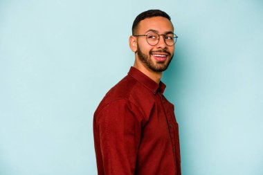 Mavi arka planda soyutlanmış genç bir İspanyol gülümsüyor, neşeli ve keyifli görünüyor..