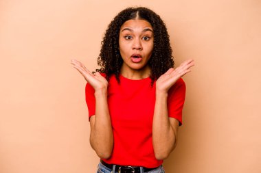 Genç Afrikalı Amerikalı kadın bej arka planda izole edilmiş. Şaşırmış ve şok olmuş..