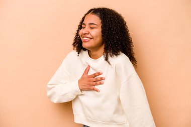 Genç Afrikalı Amerikalı kadın bej arka planda izole edilmiş. Gülüyor, elini kalbe koyuyor, mutluluk kavramını koruyor..
