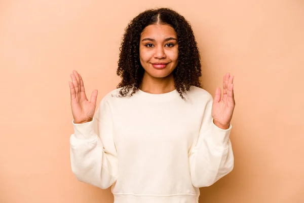 Joven Mujer Afroamericana Aislada Sobre Fondo Beige Sosteniendo Algo Poco —  Fotos de Stock