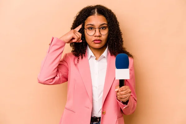 Young African American TV presenter woman isolated on beige background pointing temple with finger, thinking, focused on a task.