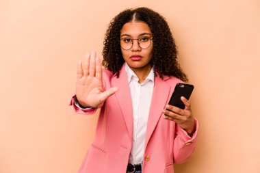Elinde bej arka planda izole edilmiş cep telefonu tutan genç Afrikalı Amerikalı kadın uzanmış elinde dur işareti ile duruyor..