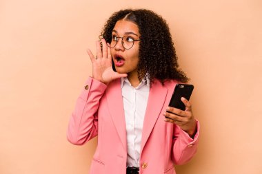 Elinde cep telefonu olan genç Afrikalı bir kadın bej arka planda izole edilmiş bağırıyor ve avuç içini açık tutuyor..