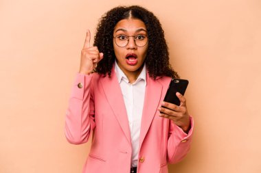 Elinde cep telefonu olan genç Afrikalı bir kadın bej arka planda izole edilmiş. Bir fikri var, ilham verici bir kavram..