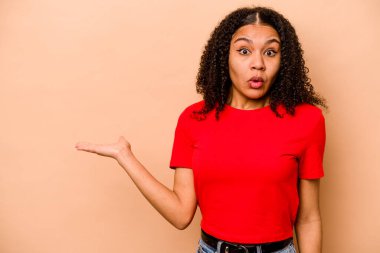 Bej arka planda izole edilmiş genç Afro-Amerikalı kadın avuç içi fotokopi alanı tutmaktan etkilenmiş..