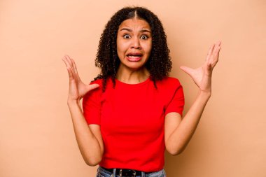 Genç Afrikalı Amerikalı kadın bej arka planda izole edilmiş gökyüzüne haykırıyor, yukarı bakıyor, hayal kırıklığına uğramış..