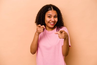 Genç Afrikalı Amerikalı kadın, bej arka planda izole edilmiş, parmaklarıyla ön tarafı işaret ediyor..