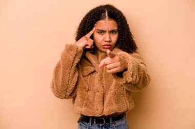 Genç Afro-Amerikalı kadın bej arka planda izole edilmiş. Parmağıyla tapınağı işaret ediyor, düşünüyor ve bir göreve odaklanıyor..
