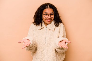 Bej arka planda izole edilmiş genç Afrikalı Amerikalı kadın kollarıyla ölçek oluşturuyor, mutlu ve kendinden emin hissediyor..
