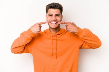 Beyaz arka planda izole edilmiş genç beyaz adam gülümsüyor, parmaklarını ağıza doğrultuyor..