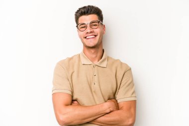 Beyaz arka planda kendini güvende hisseden, kararlılıkla kollarını kavuşturan beyaz tenli genç bir adam..