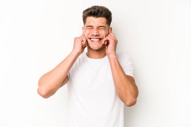 Beyaz arka planda izole edilmiş genç beyaz bir adam parmaklarıyla kulaklarını kapatıyor, gürültülü bir ortam yüzünden stresli ve çaresiz..