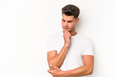 Beyaz arka planda izole edilmiş genç beyaz bir adam şüpheli ve şüpheci bir ifadeyle yana bakıyor..