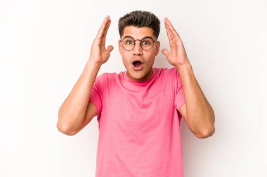 Beyaz arka planda izole olmuş genç beyaz bir adam zaferi veya başarıyı kutluyor, şaşırıyor ve şok oluyor..