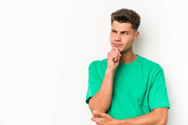 Beyaz arka planda izole edilmiş genç beyaz bir adam şüpheli ve şüpheci bir ifadeyle yana bakıyor..