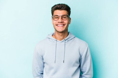 Mavi arka planda izole edilmiş genç beyaz adam mutlu, güler yüzlü ve neşeli.