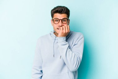Mavi arka planda izole edilmiş, tırnak yiyen, gergin ve endişeli genç bir beyaz adam..