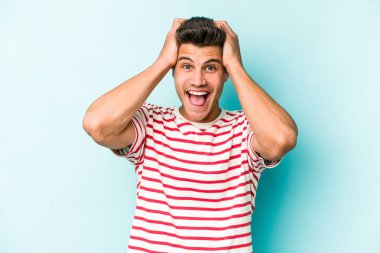 Genç beyaz adam mavi arka planda izole edilmiş bağırıyor, çok heyecanlı, tutkulu, bir şeyden memnun..