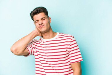 Kafkasyalı genç adam mavi arka planda izole edilmiş. Stres yüzünden boynu ağrıyor. Masaj yapıyor ve elle dokunuyor..
