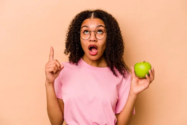 Ung Afroamerikansk Kvinna Håller Ett Äpple Isolerat Beige Bakgrund Pekar — Stockfoto