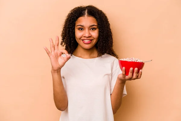 年轻的非洲裔美国女人拿着一碗谷类食品 因米色背景而被隔离 快乐而自信地摆出一副不错的姿势 — 图库照片