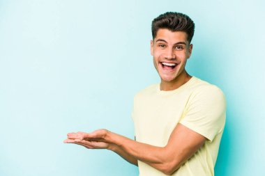 Mavi arka planda izole edilmiş genç beyaz bir adam palmiyesinde bir kopya alanı tutuyor..