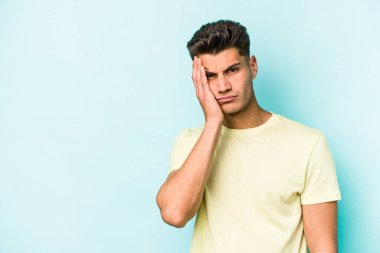 Mavi arka planda izole edilmiş, üzgün ve dalgın hisseden, kopyalama alanına bakan genç beyaz bir adam..